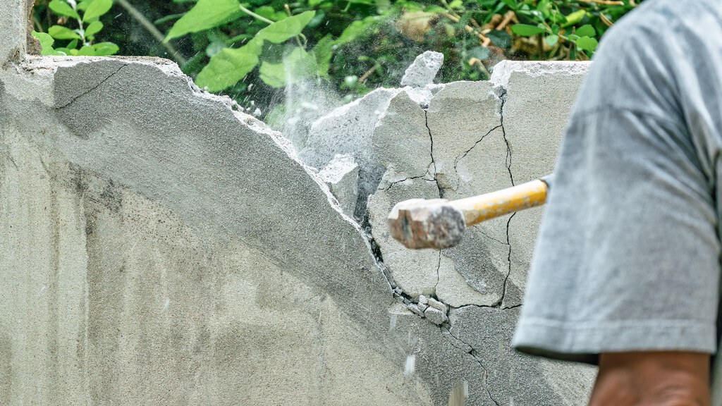 A worker using a hammer to demolish a cracked concrete wall.