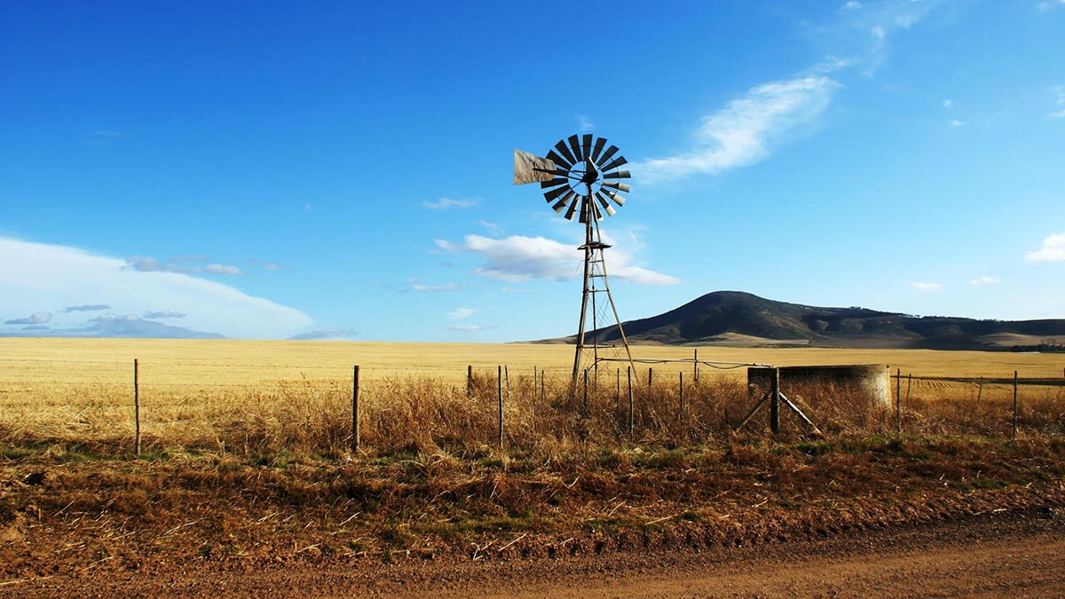 Windmill on a rural landscape with a wooden post fence.