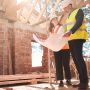 A male & female engineer standing in a semi-constructed house looking at construction plans together