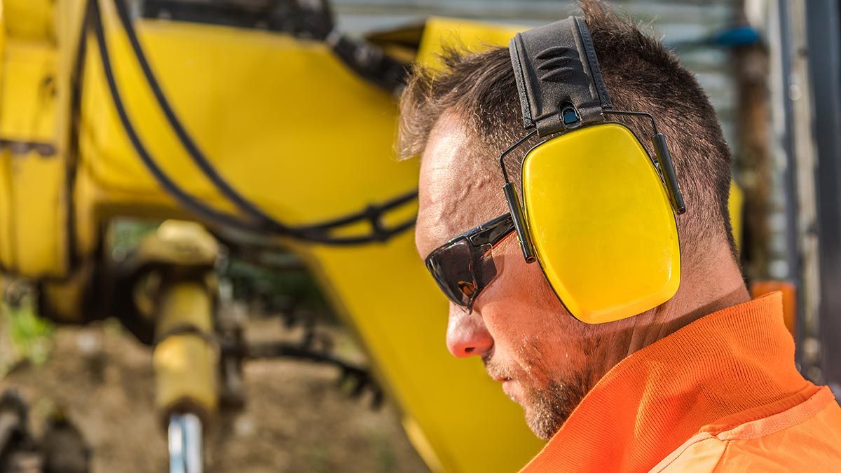 man with yellow ear muffs and safety glasses, wearing high vis