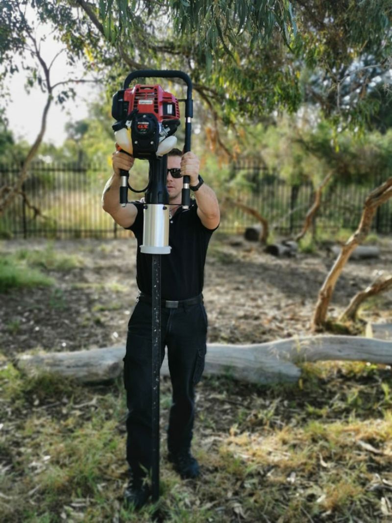 Man using Post rammer to put steel fence pole in ground